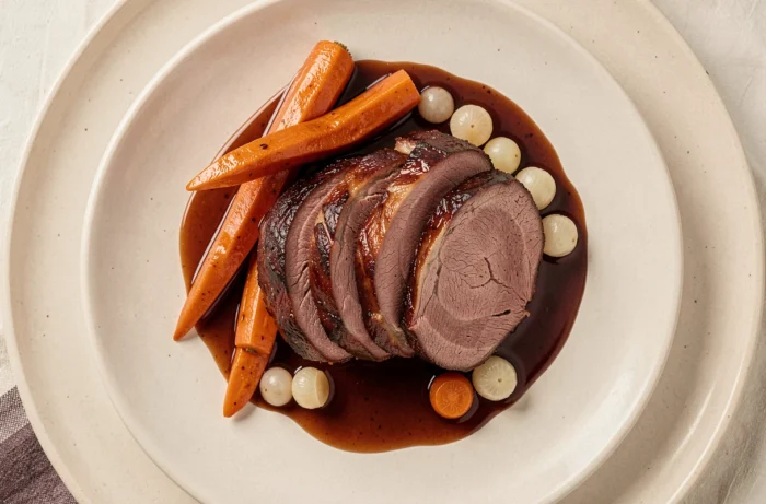 Rond de veine braisé tranché dressé sur assiette avec carottes et jus de viande en cuisine française